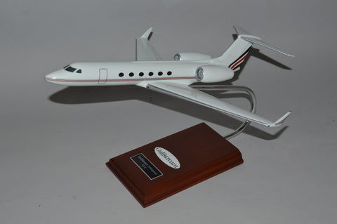A model of the Grumman Gulfstream V 500 airplane, featuring a white fuselage with red and blue accents, displayed on a wooden stand.